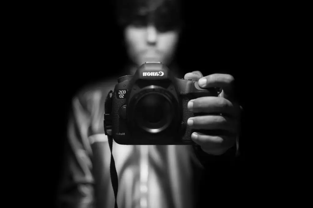 Photographer using a Canon digital camera to take a black and white self-portrait.