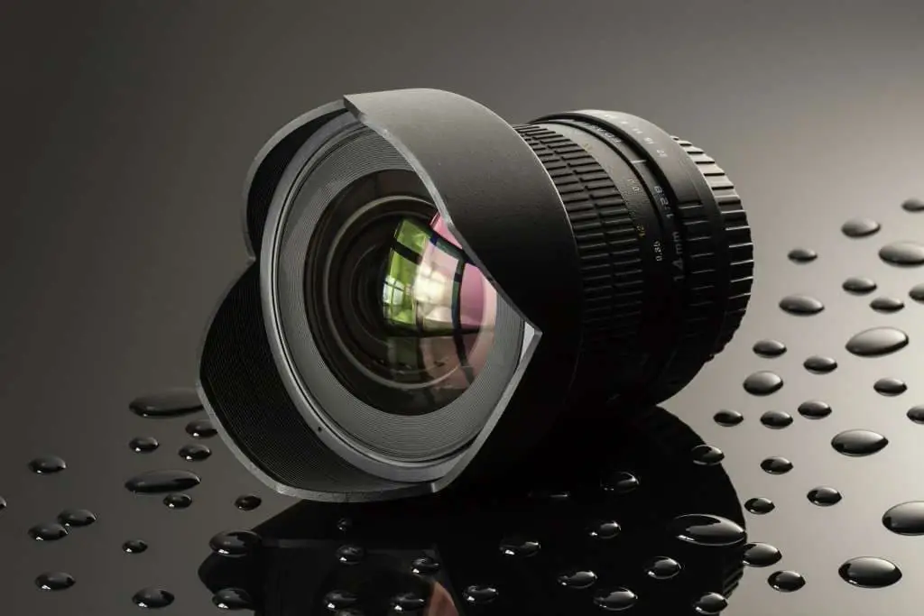 black camera lens on a glass surface with water drops