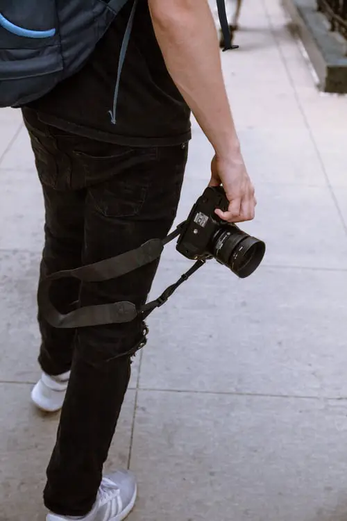 person wearing black pants wiith white shoes holding a black camera