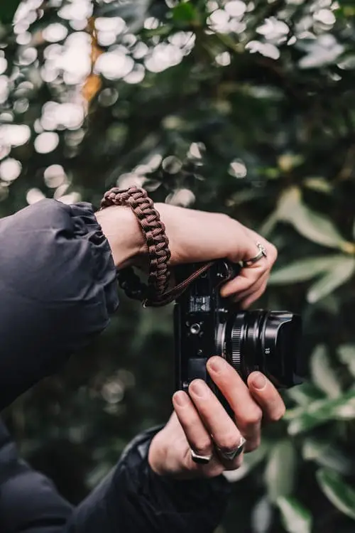 person holding a camera with green leaves on background