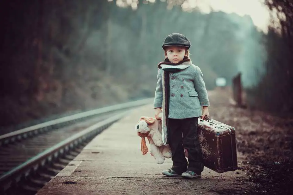 little boy holding a teddy bear and a suitcase
