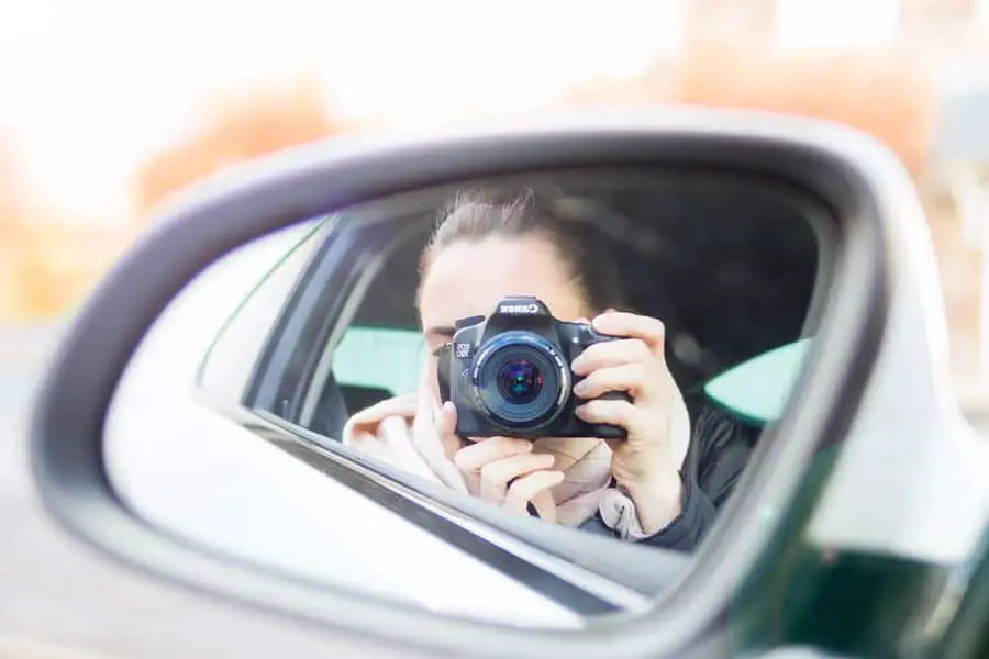 Woman taking a photo of herself through a car mirror