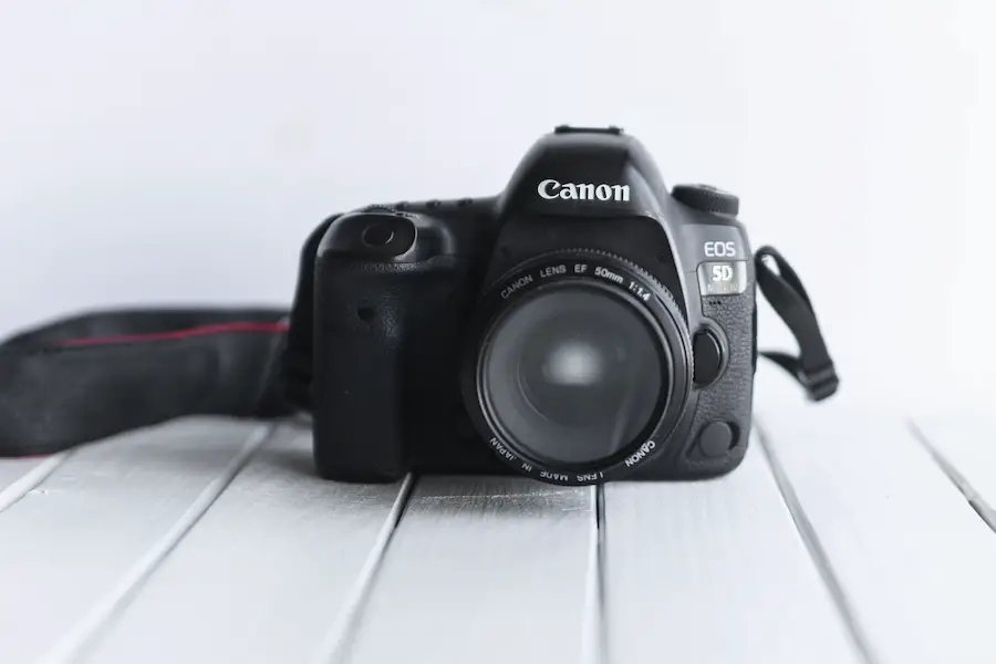 Black Canon DSLR camera on white wooden surface