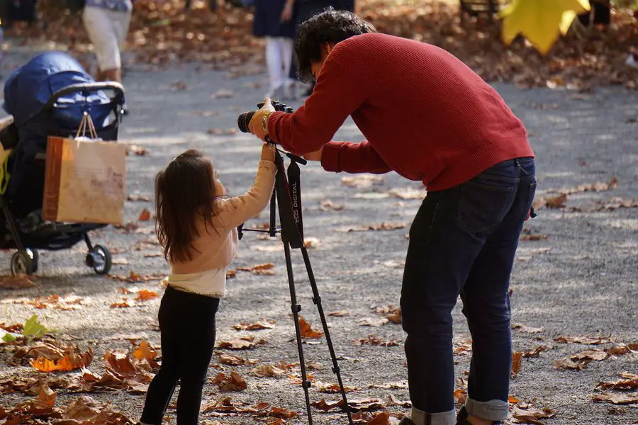 Photographer adjusting his camera on a tripod, while a little girl tries to help