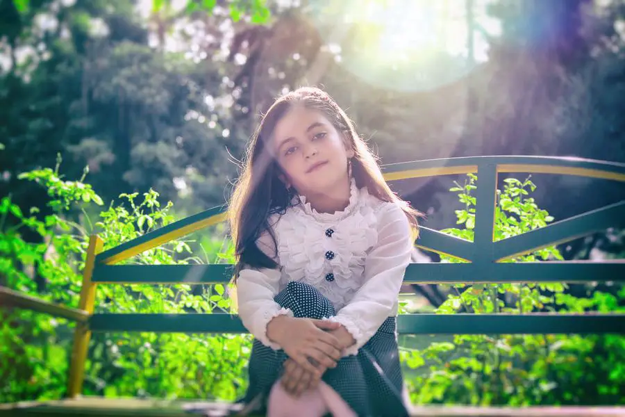 Little girl sitting on a bench with a strong sunlight seen in the background